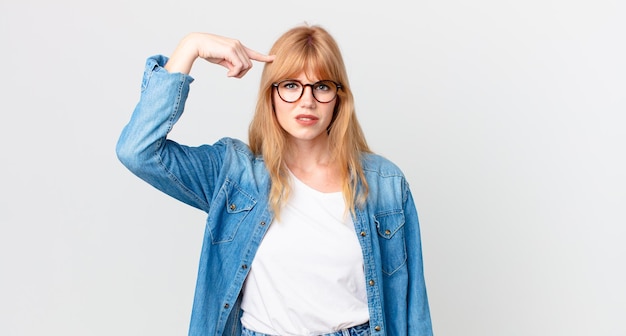 Jolie femme à tête rouge se sentant confuse et perplexe, vous montrant que vous êtes fou