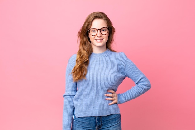 jolie femme tête rouge souriant joyeusement avec une main sur la hanche et confiante