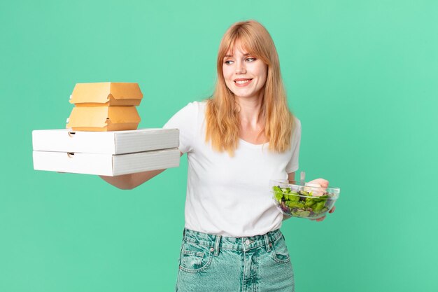 Jolie femme à tête rouge tenant des boîtes de restauration rapide et une salade