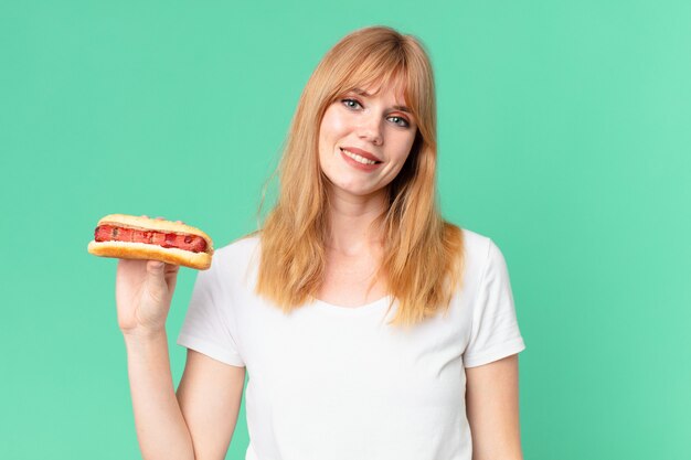 Jolie femme tête rouge tenant un hot-dog.