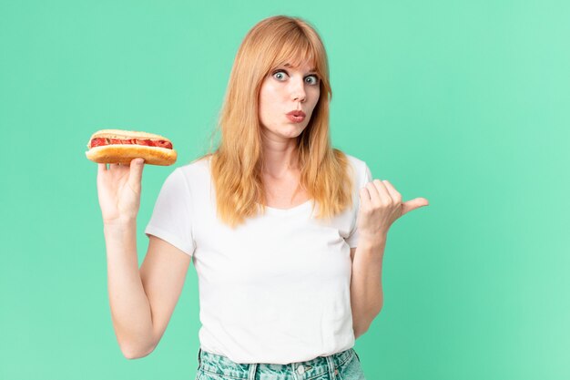 Jolie femme tête rouge tenant un hot-dog.