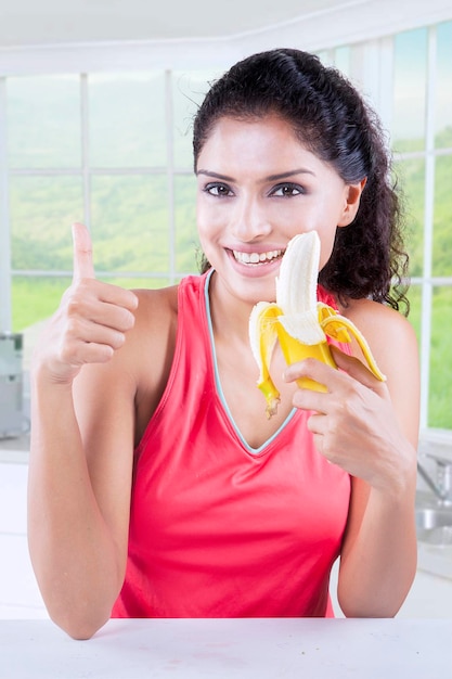 Une jolie femme tient une banane dans la cuisine.