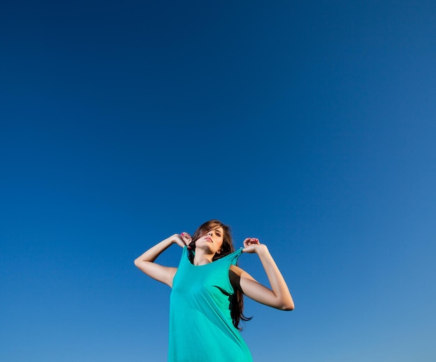 La jolie femme tire des courroies de sa robe bleue contre le ciel bleu