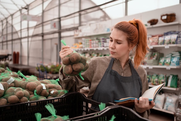 Jolie femme travaillant dans l'entrepôt du centre commercial de jardinage et faisant du contrôle de la qualité de la pomme de terre pour la culture