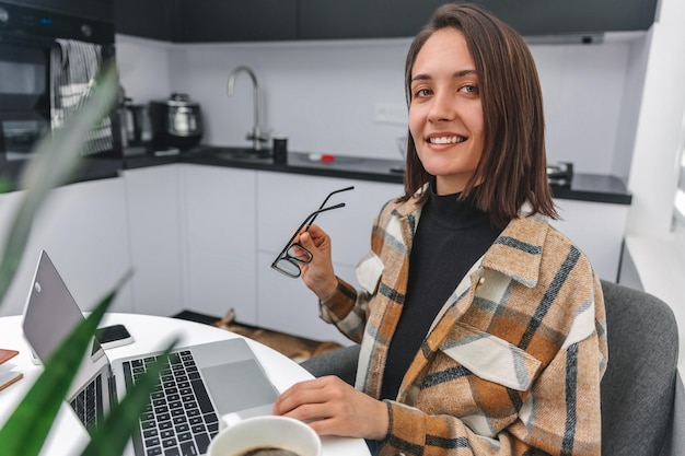 Jolie femme travaillant sur son ordinateur portable à la maison et regardant la caméra