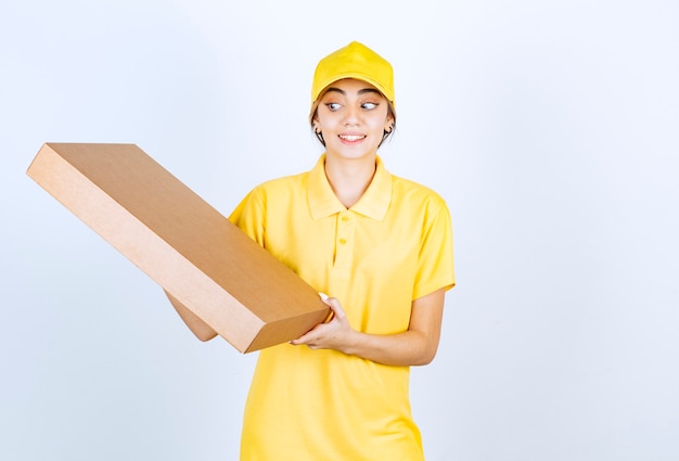 Une jolie femme en uniforme jaune tenant une boîte de papier kraft vierge marron.