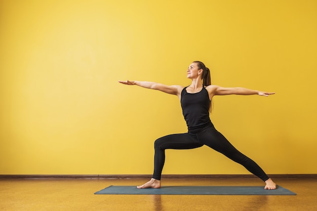 Jolie femme en vêtements de sport noirs pratiquant le yoga effectue une posture de guerrier exercice virabhadrasana