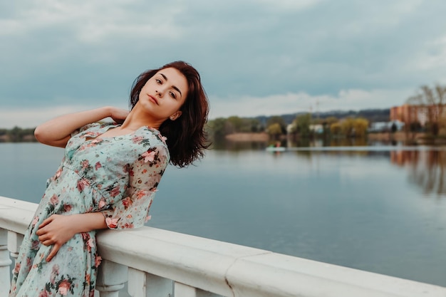 Jolie femme vêtue d'une robe fleurie debout sur la jetée près du lac de la rivière moody temps nuageux