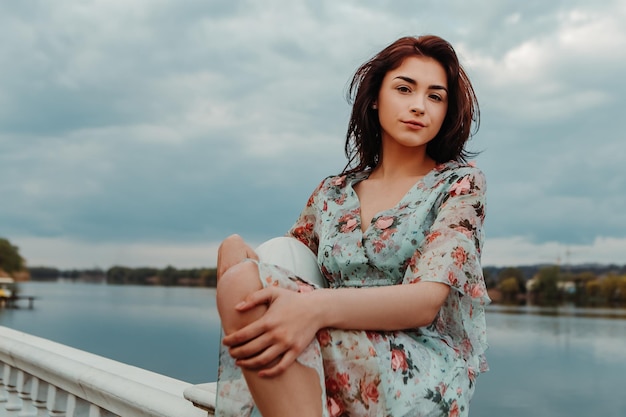 Jolie femme vêtue d'une robe fleurie debout sur la jetée près du lac de la rivière moody temps nuageux