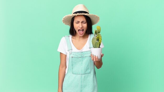 Jolie fermière criant agressivement, l'air très en colère et tenant un cactus