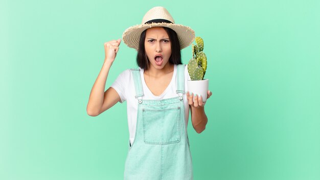 Jolie fermière criant agressivement avec une expression de colère et tenant un cactus