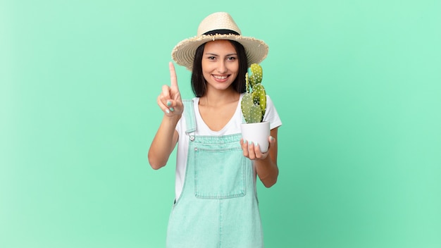 Jolie fermière souriante fièrement et avec confiance faisant le numéro un et tenant un cactus