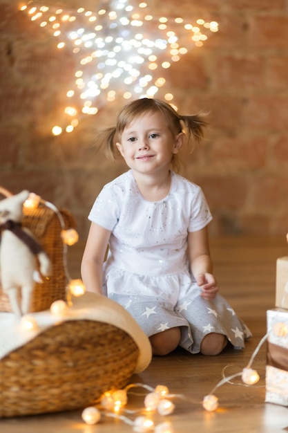 Jolie fille de 4 ans assise sur le sol parmi les guirlandes du nouvel an.