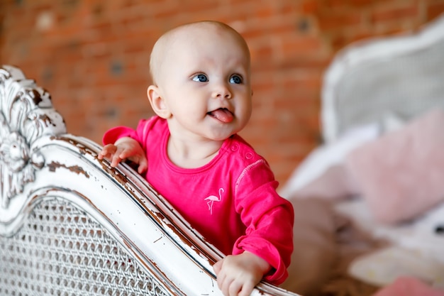 Jolie fille de 6 mois aux yeux bleus heureux en robe rouge vif à la tête du lit rétro