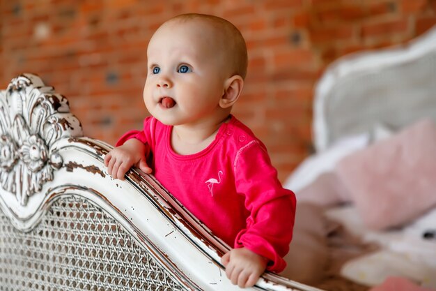 Jolie fille de 6 mois aux yeux bleus heureux en robe rouge vif à la tête du lit rétro