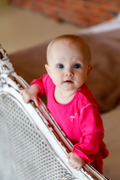 Jolie fille de 6 mois aux yeux bleus heureux en robe rouge vif à la tête du lit rétro