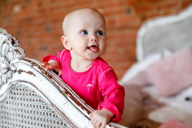 Jolie fille de 6 mois aux yeux bleus heureux en robe rouge vif à la tête du lit rétro