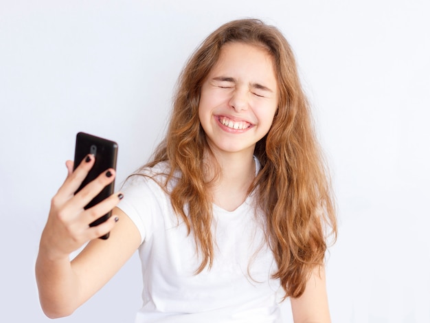 Jolie fille adolescente aux cheveux longs rend selfie drôle avec le visage qui rit
