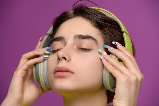 Jolie fille affectueuse avec une coupe de cheveux courte et un nail art extravagant portant des écouteurs