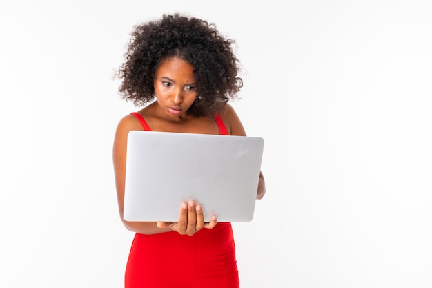 Photo jolie fille africaine tenant un ordinateur portable ouvert et en tapant soigneusement sur un clavier sur un mur blanc