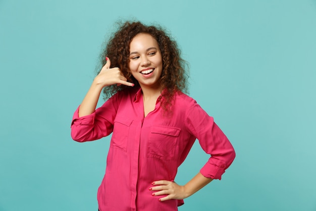 Jolie fille africaine en vêtements décontractés faisant un geste téléphonique comme dit de me rappeler, regardant de côté isolé sur fond bleu turquoise. Les gens émotions sincères, concept de style de vie. Maquette de l'espace de copie.