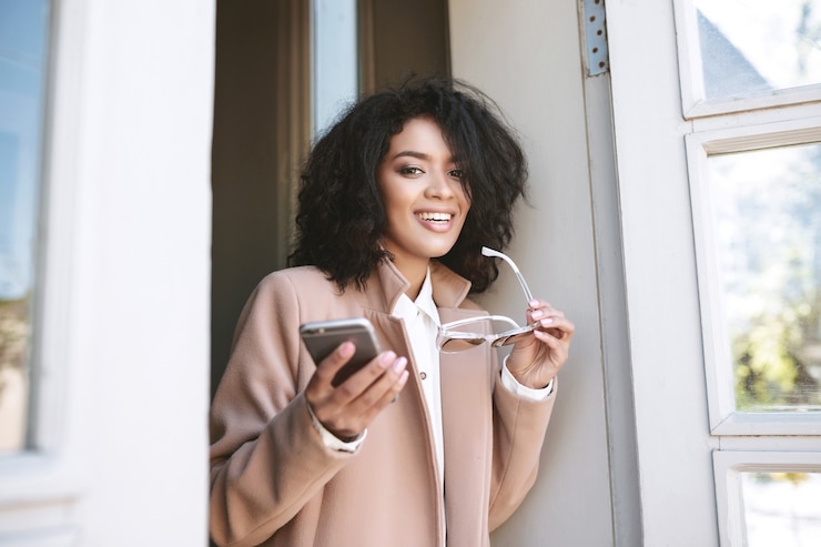 Photo jolie fille afro-américaine debout avec téléphone portable et lunettes de soleil dans les mains