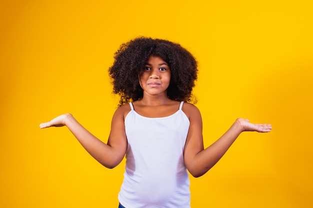 Jolie fille afro sur une expression confuse et un arrière-plan isolé désemparé avec les bras et les mains levées. Notion de doute.