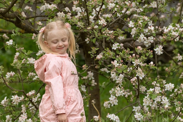 Photo une jolie fille d'âge préscolaire avec les yeux fermés porte une tenue rose clair debout près d'un arbre en fleurs dans le jardin de printemps