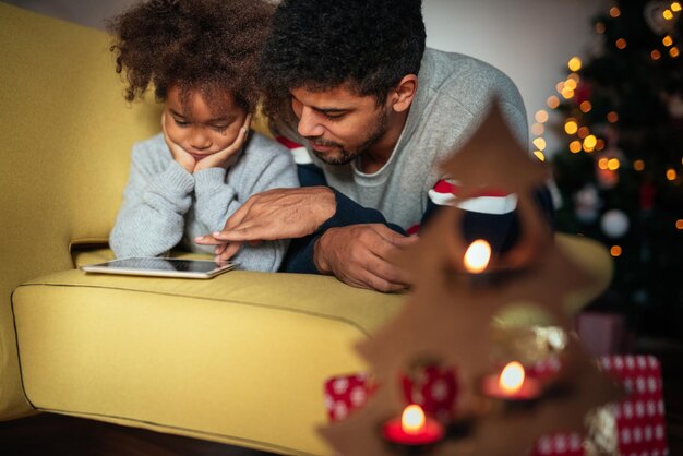 Jolie fille à l'aide de tablette avec papa à la maison