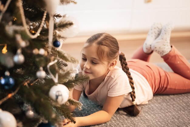 Jolie fille allongée et souriante près de l'arbre de Noël. Notion de Noël.