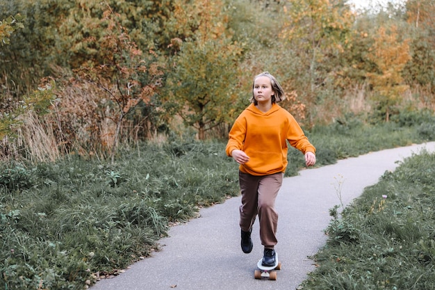 Jolie fille apprenant à faire de la planche à roulettes à l'extérieur par une belle journée d'automne. Activités pour enfants et concept de mode de vie actif.