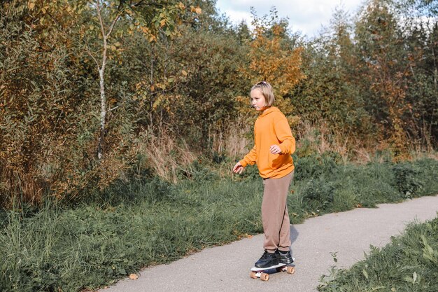 Jolie fille apprenant à faire de la planche à roulettes à l'extérieur par une belle journée d'automne. Activités pour enfants et concept de mode de vie actif.