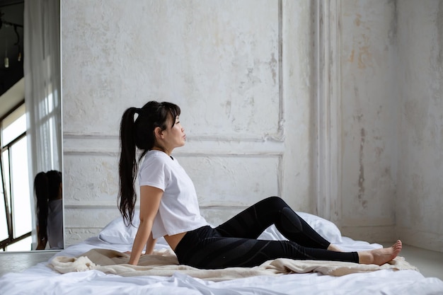 jolie fille asiatique aux cheveux longs noirs est assise sur le lit le matin se penchant en arrière