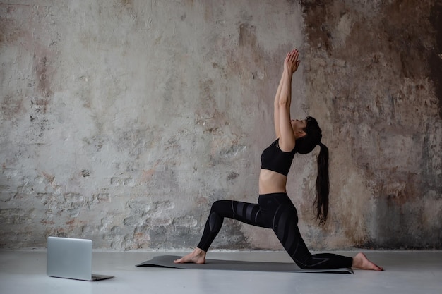 jolie fille asiatique aux cheveux longs noirs en vêtements de sport d'entraînement faisant du yoga en ligne à l'aide d'un ordinateur portable