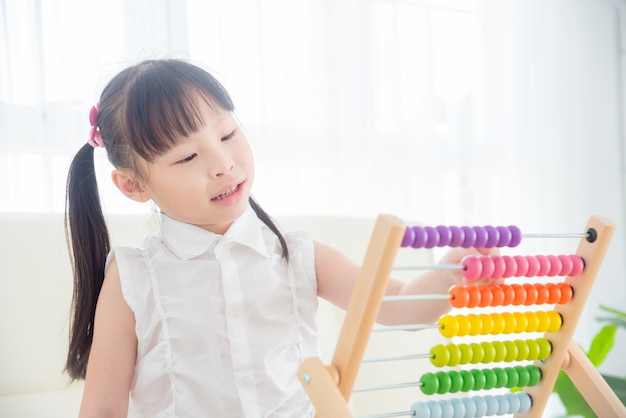 Jolie fille asiatique comptant du bois sur un boulier à la maison. Concept d'éducation des enfants.