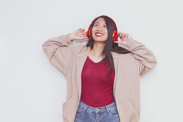 Jolie fille asiatique écoute de la musique avec un casque rouge sur fond blanc.