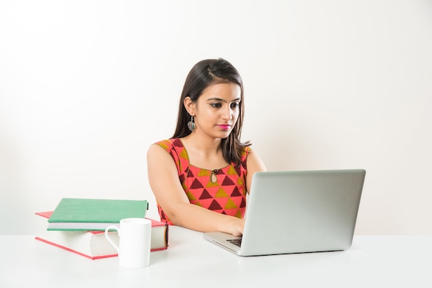 Jolie fille asiatique indienne étudiant sur un ordinateur portable avec une pile de livres sur la table, sur fond blanc