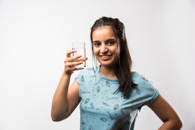 Jolie fille asiatique indienne tenant un verre d'eau plate, debout isolé sur fond blanc