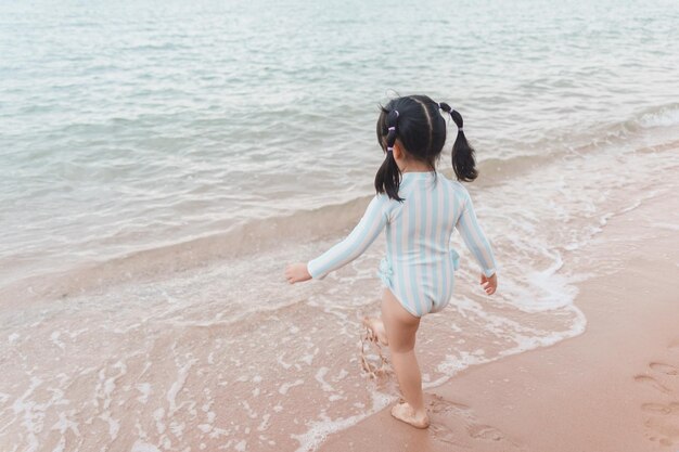 Jolie fille asiatique marchant ou courant ou jouant sur la plage pendant les vacances d'été Enfants avec beau sable de mer et ciel bleu Enfants heureux en vacances au bord de la mer courant sur la plage