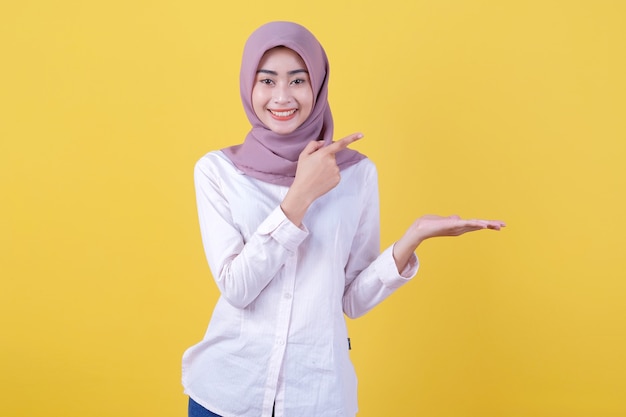 Jolie fille asiatique montrant quelque chose à portée de main portant le hijab