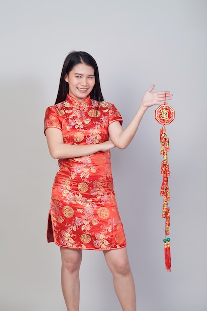 Jolie fille asiatique avec une robe traditionnelle chinoise cheongsam ou qipao tenant un pétard. Concept de nouvel an chinois, modèle féminin isolé sur fond gris studio