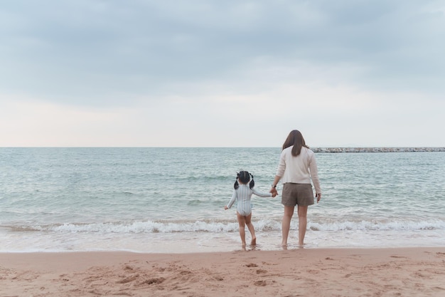 Jolie fille asiatique et sa mère marchant ou courant ou jouant sur la plage pendant les vacances d'été Enfants avec beau sable de mer et ciel bleu Enfants heureux en vacances au bord de la mer courant sur la plage