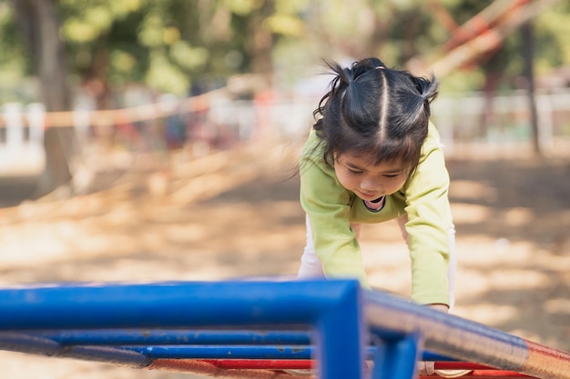 Jolie fille asiatique sourire jouer grimper la barre sur la cour ou l'aire de jeux de l'école ou de la maternelle Activité saine enfants Petite fille grimpant à l'extérieur sur l'aire de jeux Enfant jouant sur l'aire de jeux extérieure