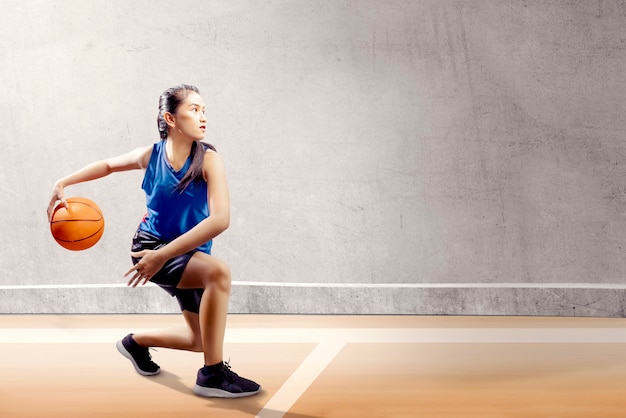 Jolie fille asiatique en uniforme de sport bleu sur pivot de basket bouge sur le terrain de basket