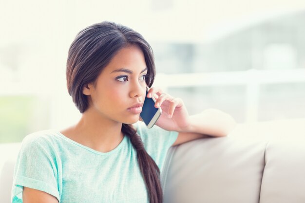 Jolie fille assise sur le canapé en téléphonant