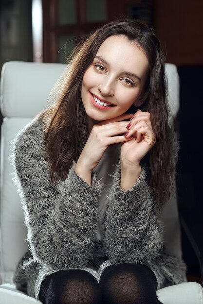 Jolie fille assise avec les mains près de son menton, souriant et écoutant attentivement