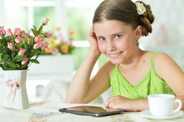 Jolie fille assise à table et utilisant une tablette numérique