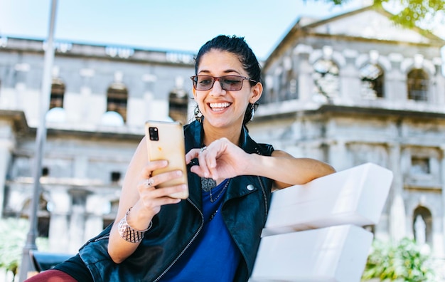 Une jolie fille assise sur le téléphone portable en souriant Fille assise sur un banc envoyant des SMS sur son téléphone portable Fille de style urbain assise sur un banc avec son téléphone portable