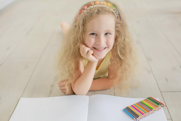 une jolie fille aux cheveux bouclés et aux yeux bleus dessine dans un album avec des crayons de couleur