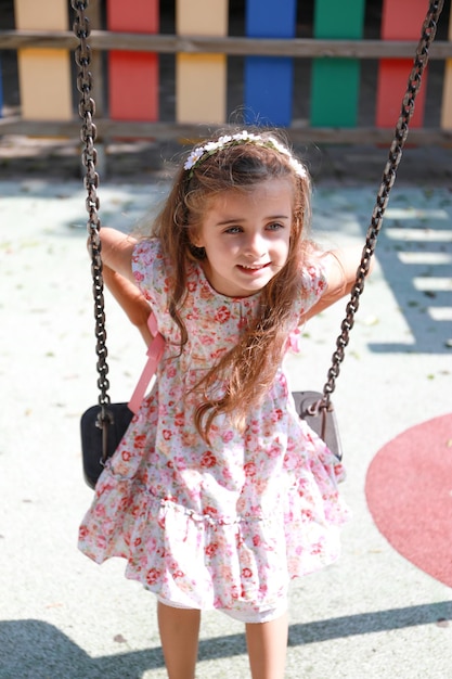 une jolie fille aux cheveux bruns et aux yeux vert clair, heureuse et souriante sur une balançoire à Alicante